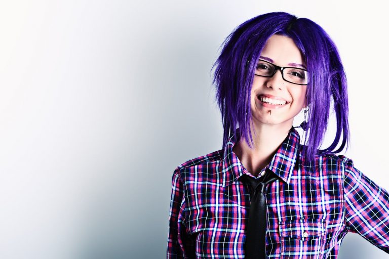 Emo punk girl with purple hair and black thick framed glasses wearing a stud and dangling earring, plaid shirt and black tie