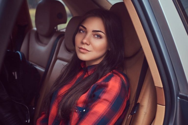 Caucasian woman wearing a black and red flannel shirt sitting in a car not smiling