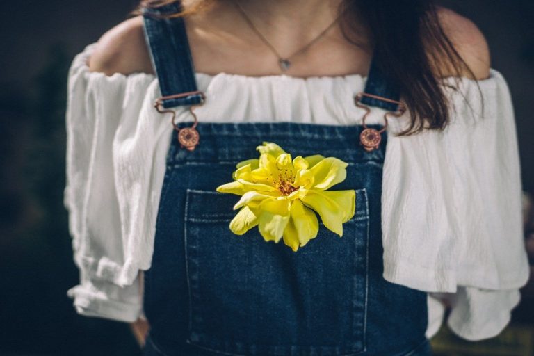 woman wearing denim blue overalls with a yellow flower in the pocket